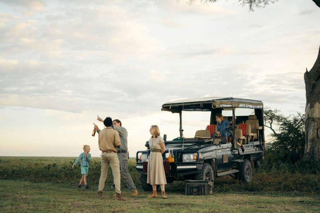 People gathered around a safari vehicle in a grassy field.